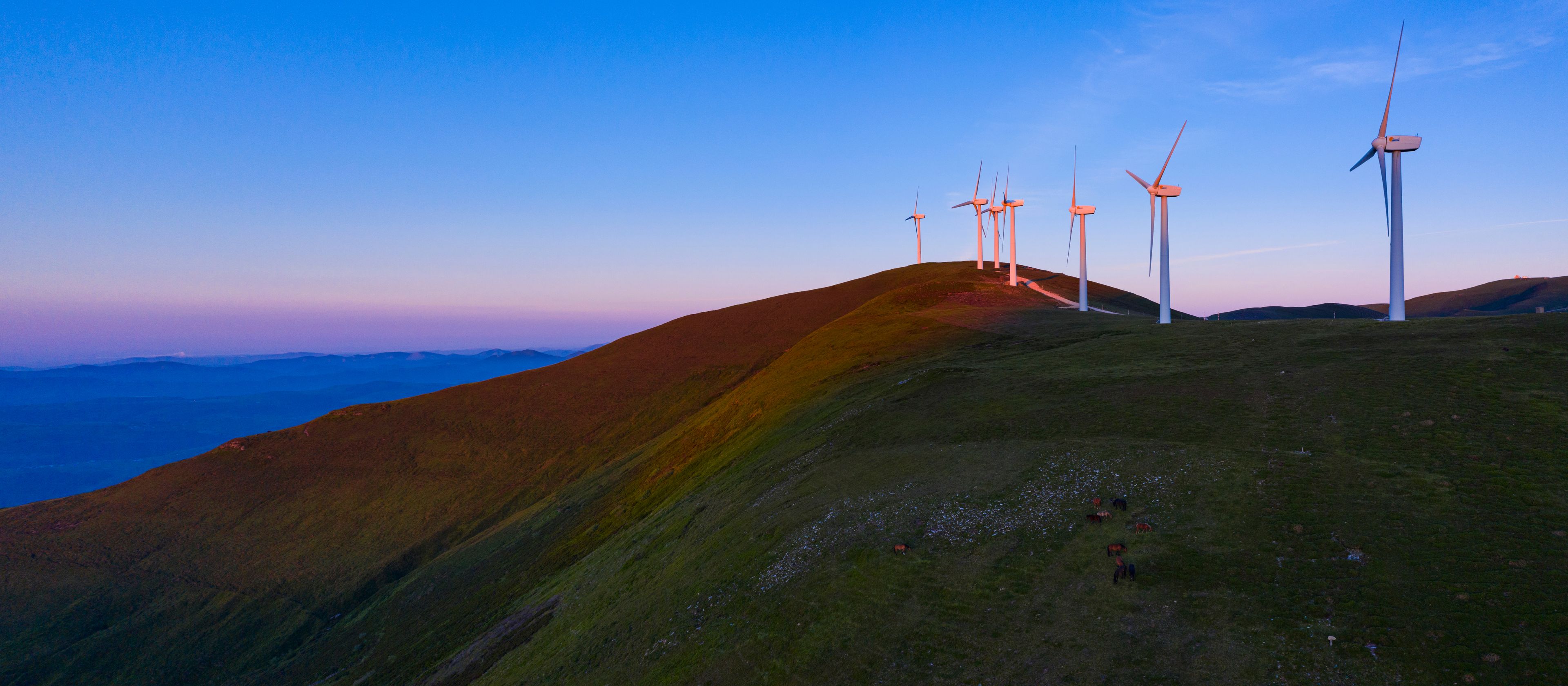 Paisagem com várias turbinas eólicas numa colina.
