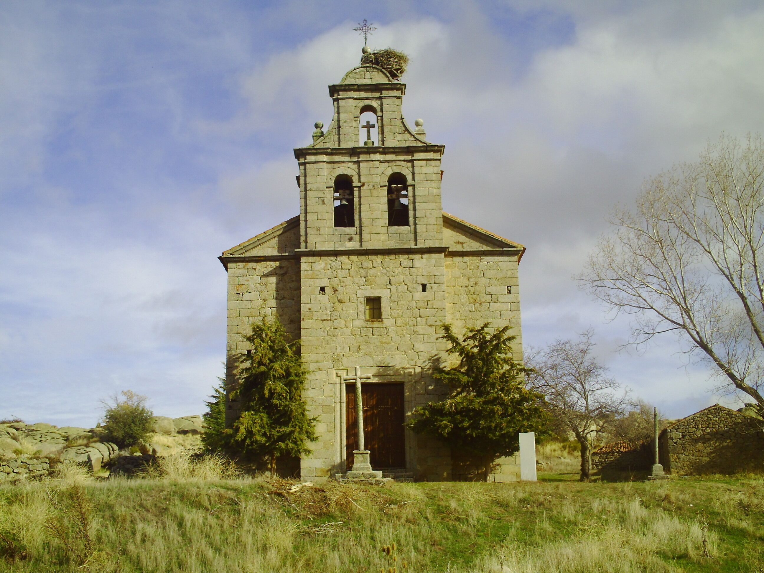 A stone church with a bell tower and crosses, surrounded by grass and trees.