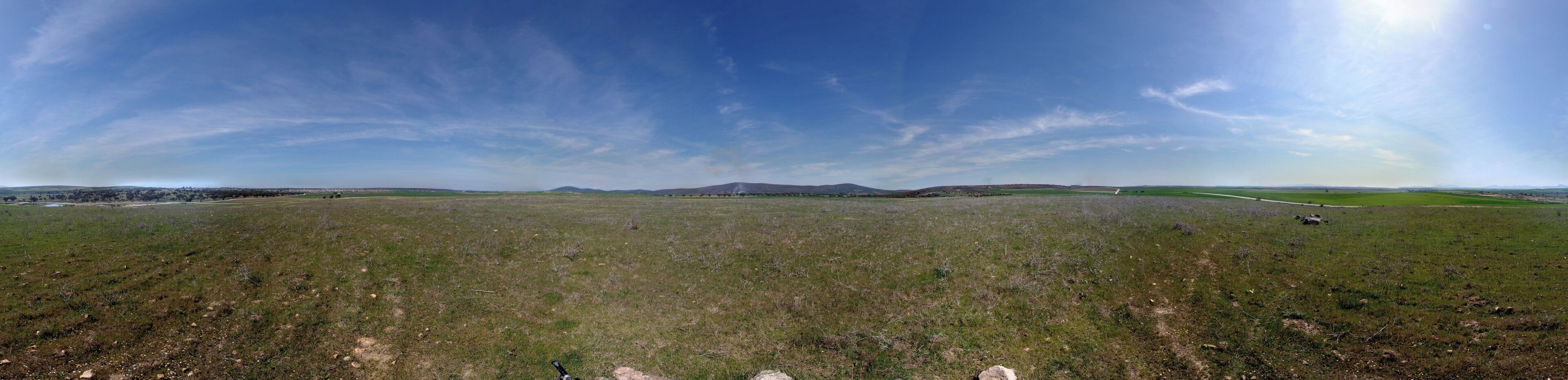 A wide-open field with a clear sky, distant mountains, and a road curving through the landscape.
