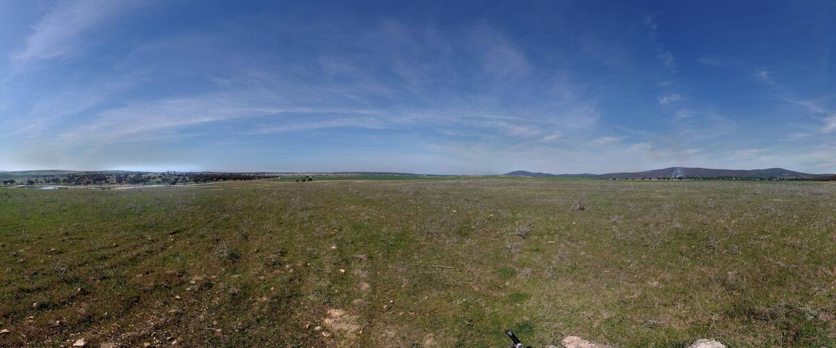 A wide-open field with a clear sky, distant mountains, and a road curving through the landscape.