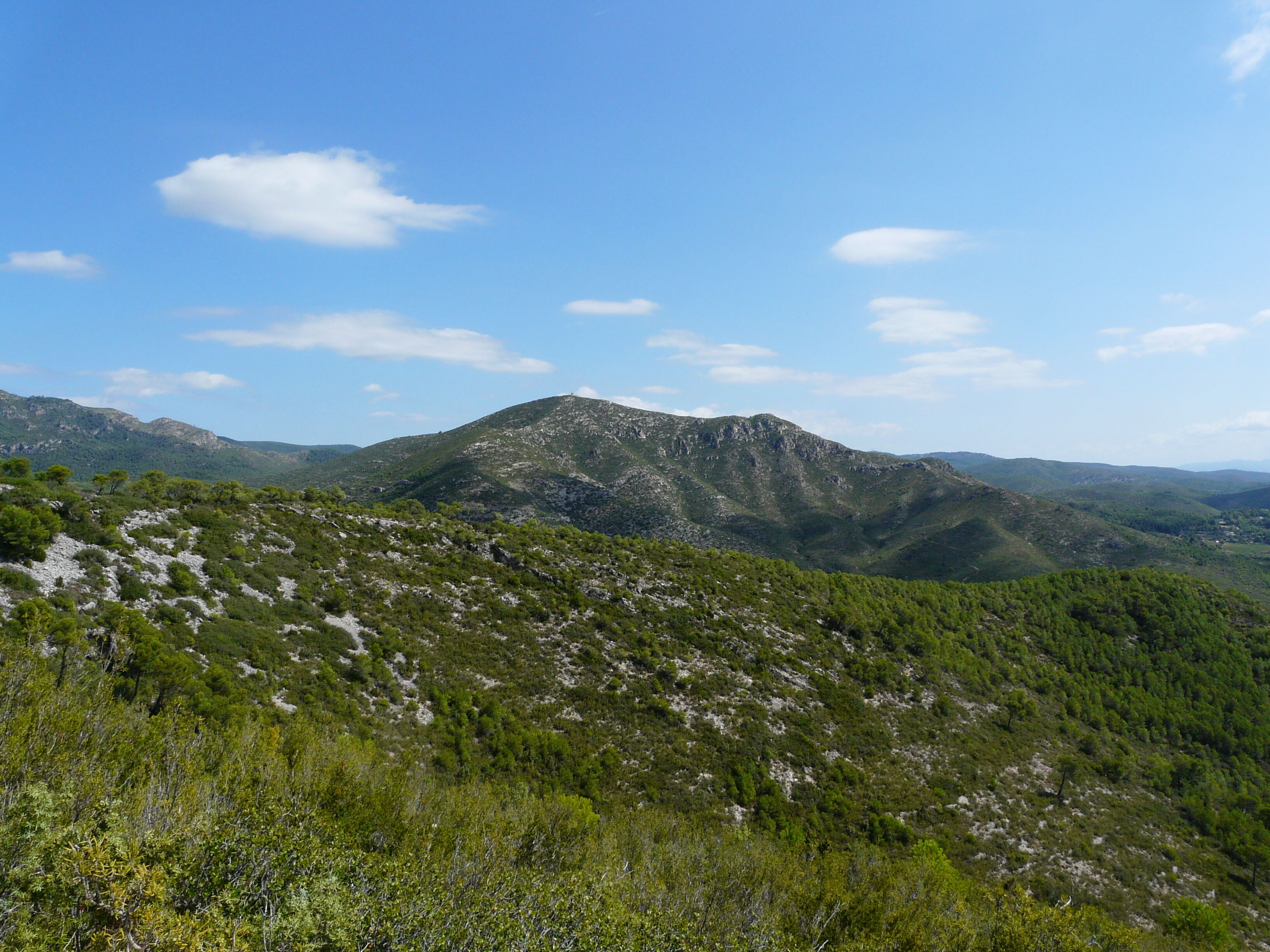 A mountainous landscape with dense green vegetation and rocky terrain under a clear blue sky.