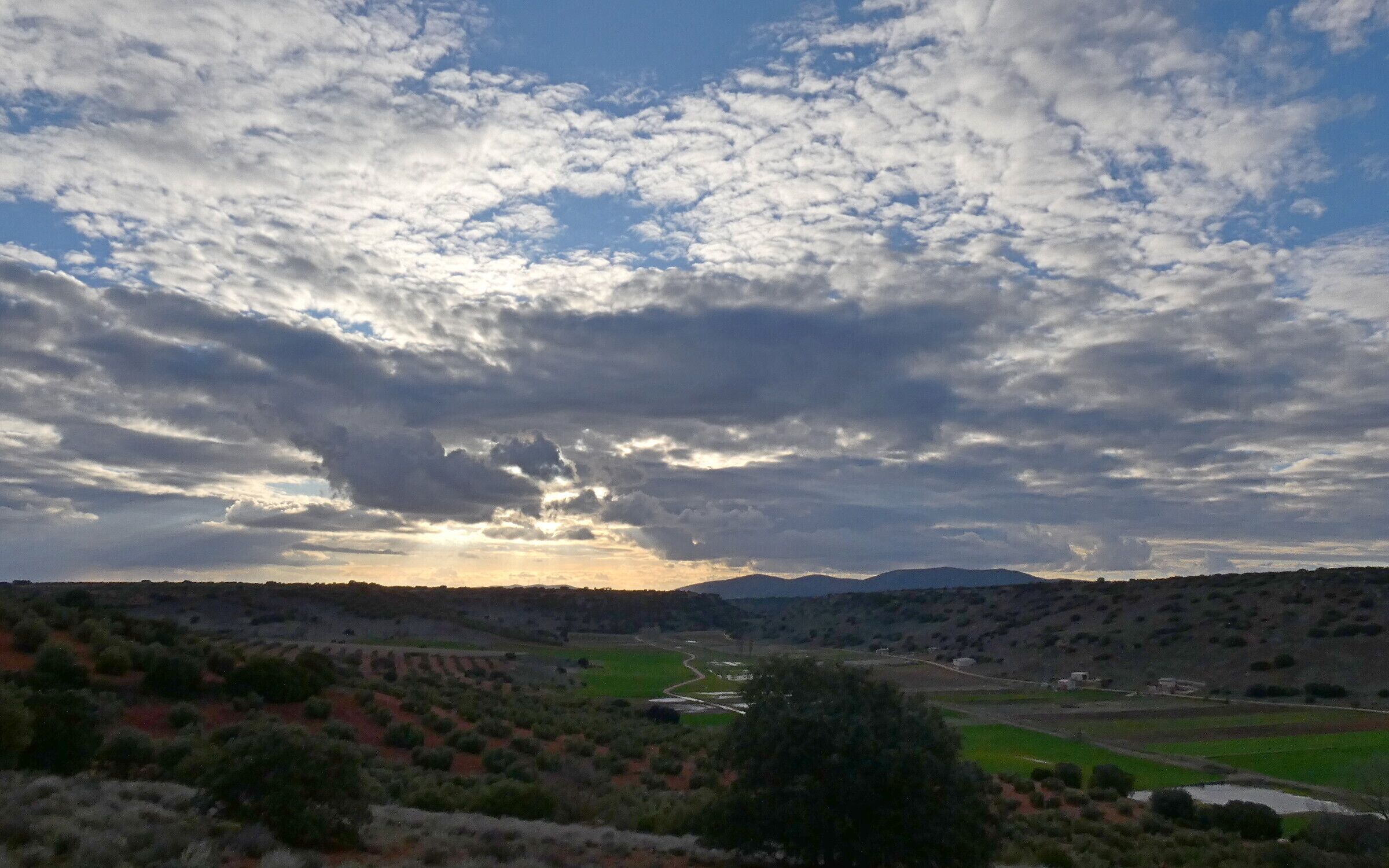A valley with a river, green fields, and distant mountains under a cloudy sky.