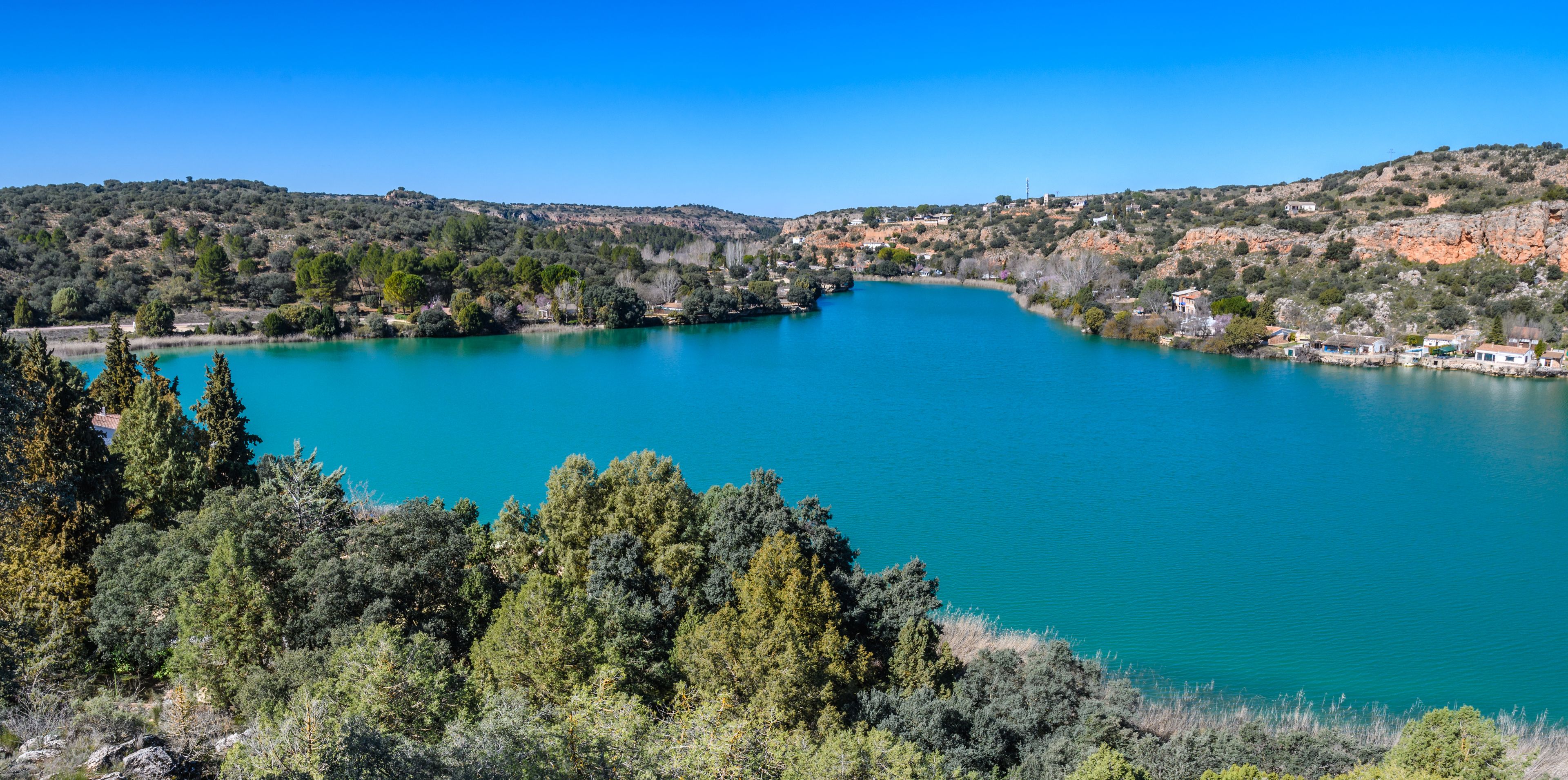 Un lago turquesa rodeado de colinas y árboles.
