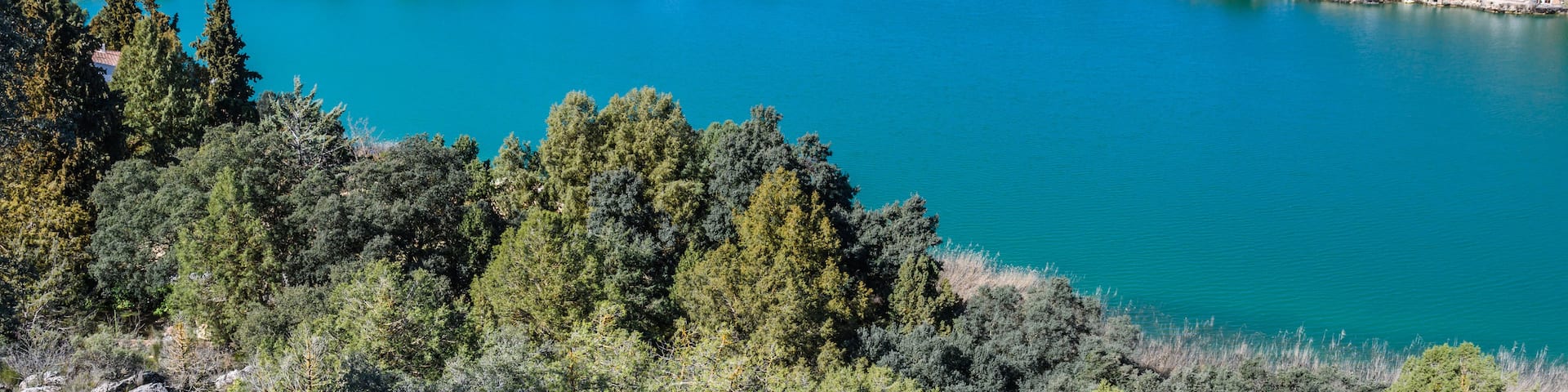 A turquoise lake surrounded by hills and trees.
