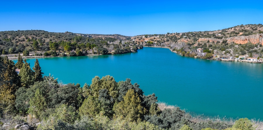 Un lago turquesa rodeado de colinas y árboles.