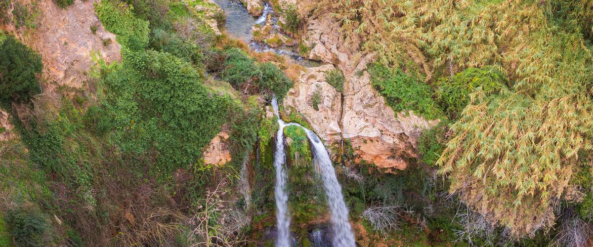 A waterfall cascading into a river surrounded by dense vegetation and rocky terrain.