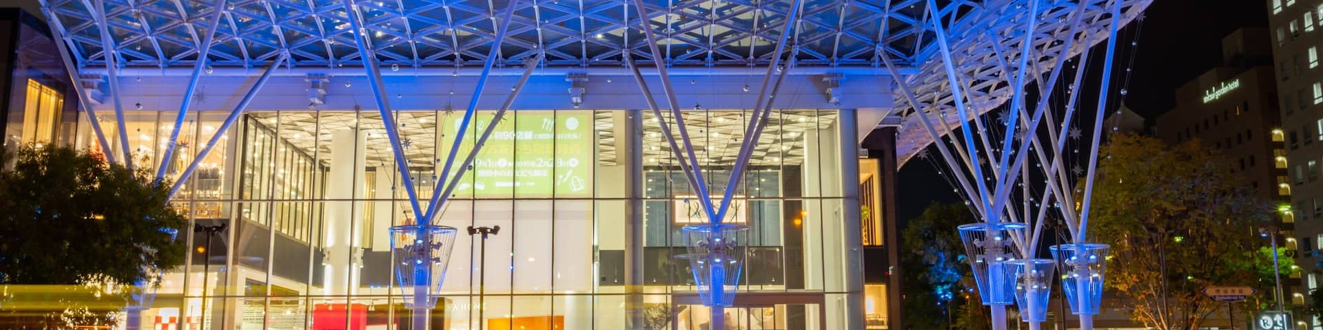 The exterior of AEON Mall with a distinctive roof structure and illuminated signage.
