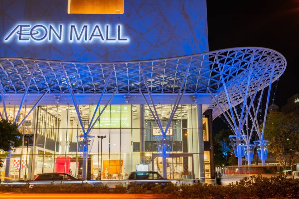 Exterior del centro comercial AEON con una estructura de techo distintiva y señalización iluminada.