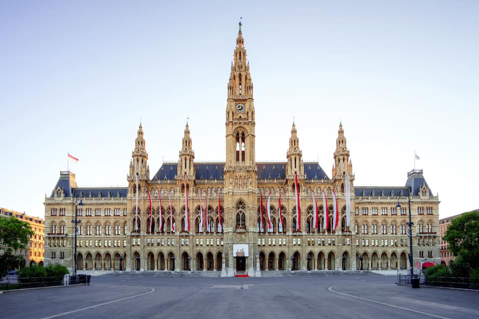 A grand historic building with a tall central tower, multiple spires, and a series of flags.