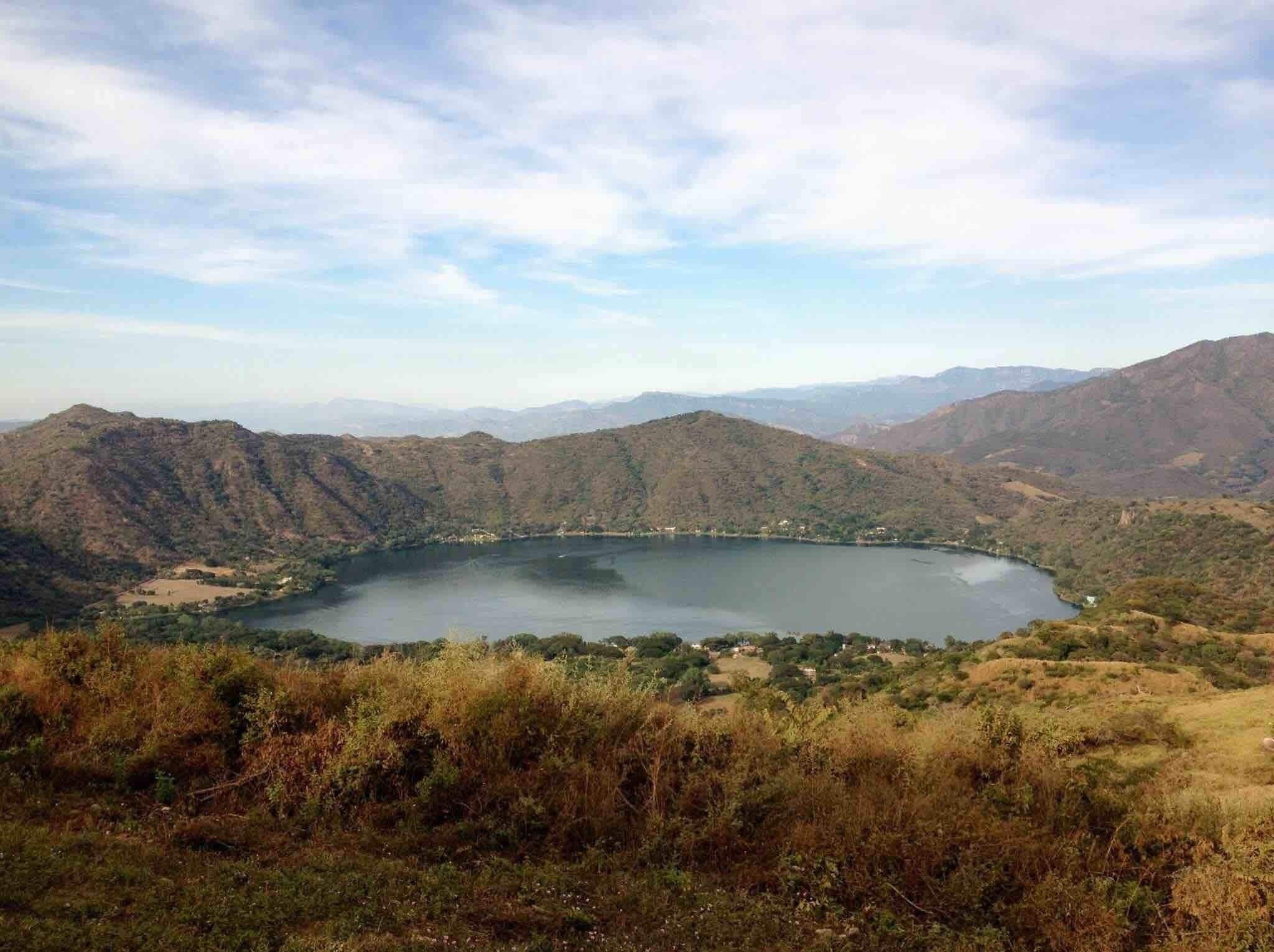 A lake surrounded by hills with sparse vegetation and a clear sky.