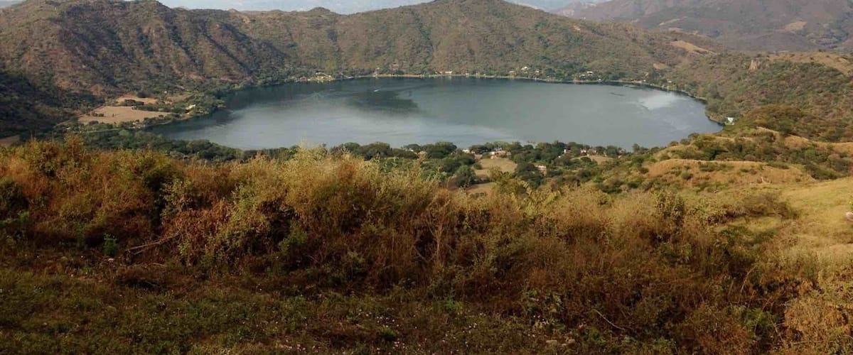 A lake surrounded by hills with sparse vegetation and a clear sky.