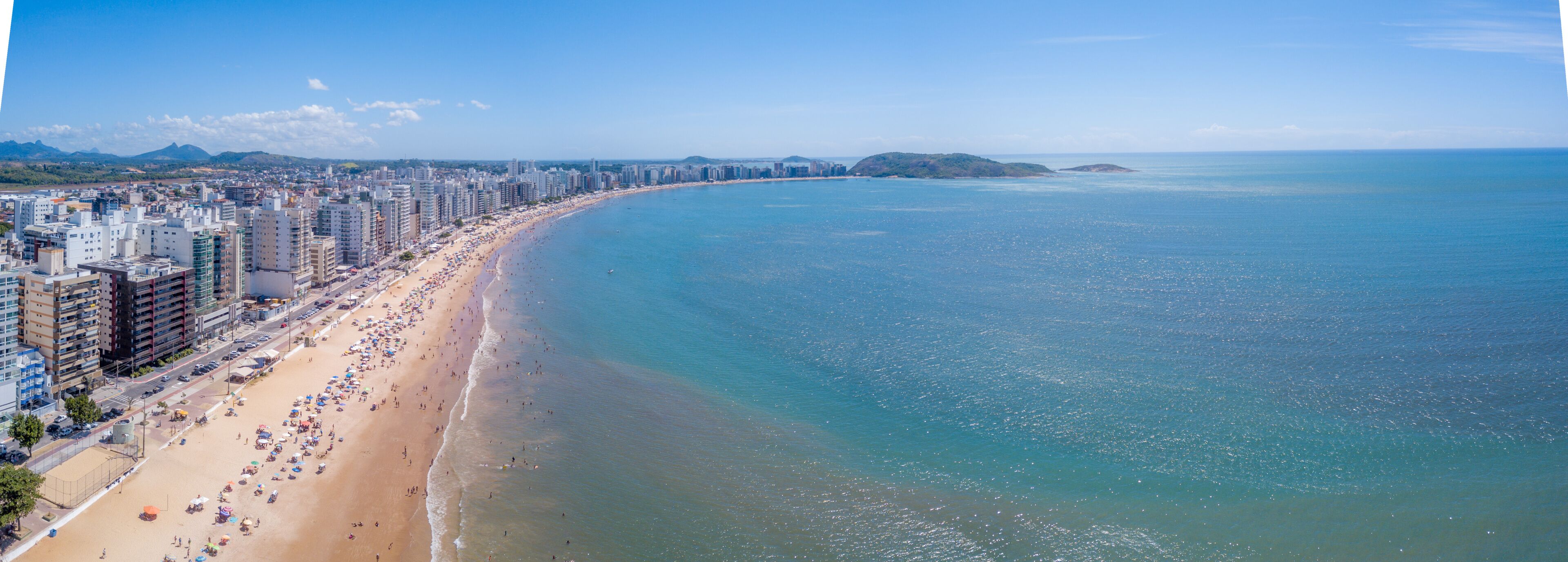 A coastal cityscape with a long beach, high-rise buildings, and distant islands.