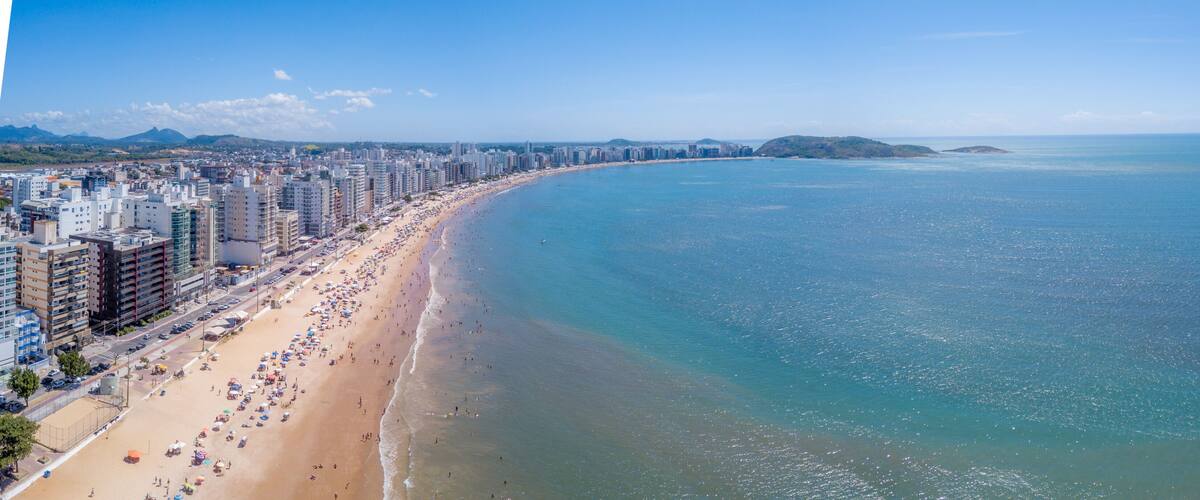 A coastal cityscape with a long beach, high-rise buildings, and distant islands.
