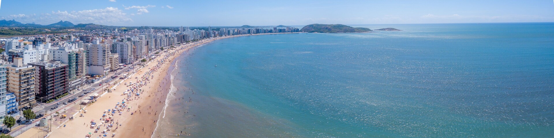 A coastal cityscape with a long beach, high-rise buildings, and distant islands.