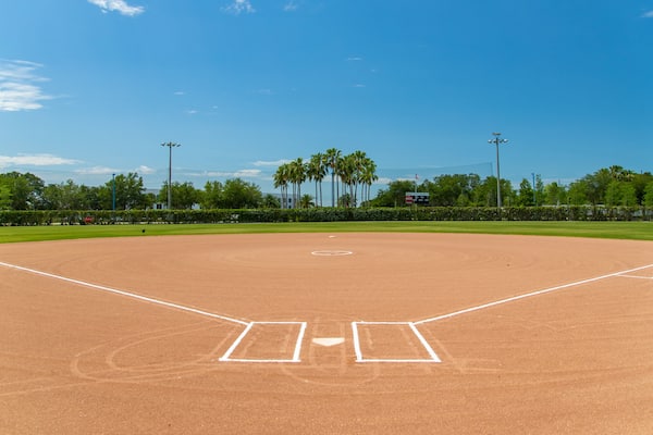 En baseballbane med klar himmel, palmer og en pointtavle.