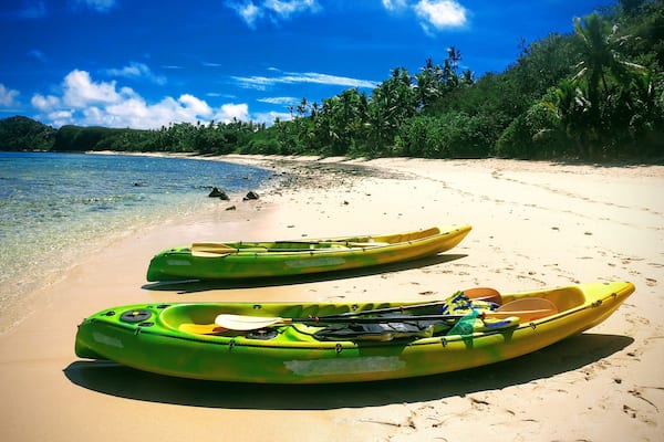 Deux kayaks sur une plage de sable, avec une eau d’un bleu limpide et une forêt en arrière-plan.