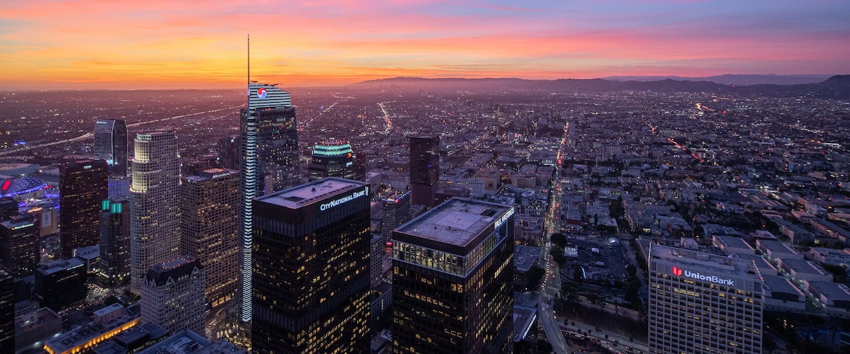 A cityscape at dusk with illuminated skyscrapers and a sunset sky.