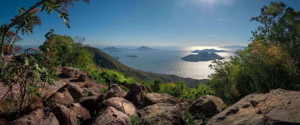 A mountainous landscape with rocky terrain, lush greenery, and a view of the ocean with distant islands.