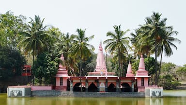Een tempel met een centrale spits en twee kleinere spitsen, omgeven door palmbomen en een waterpartij.