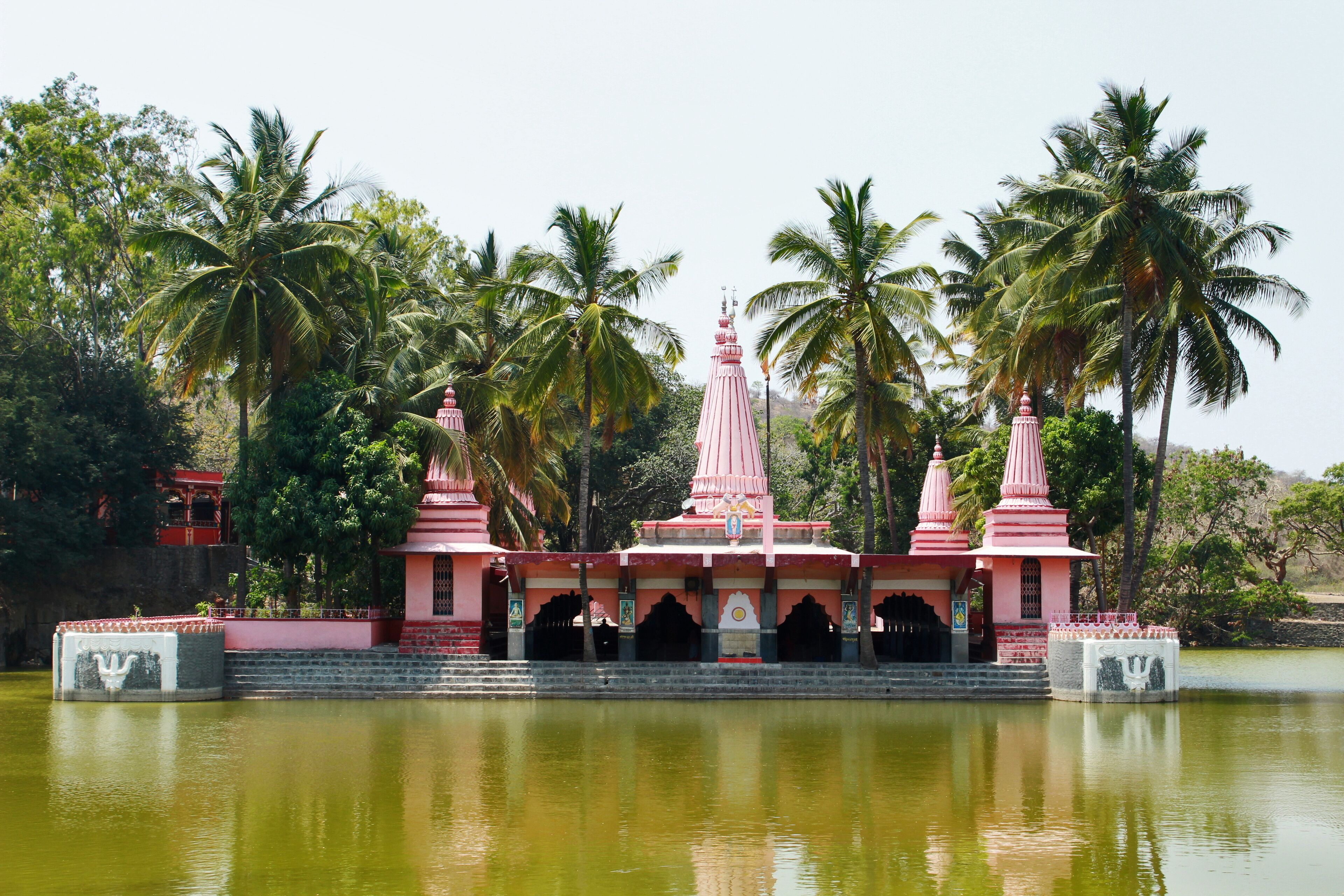 A temple with a central spire and two smaller spires, surrounded by palm trees and a body of water.