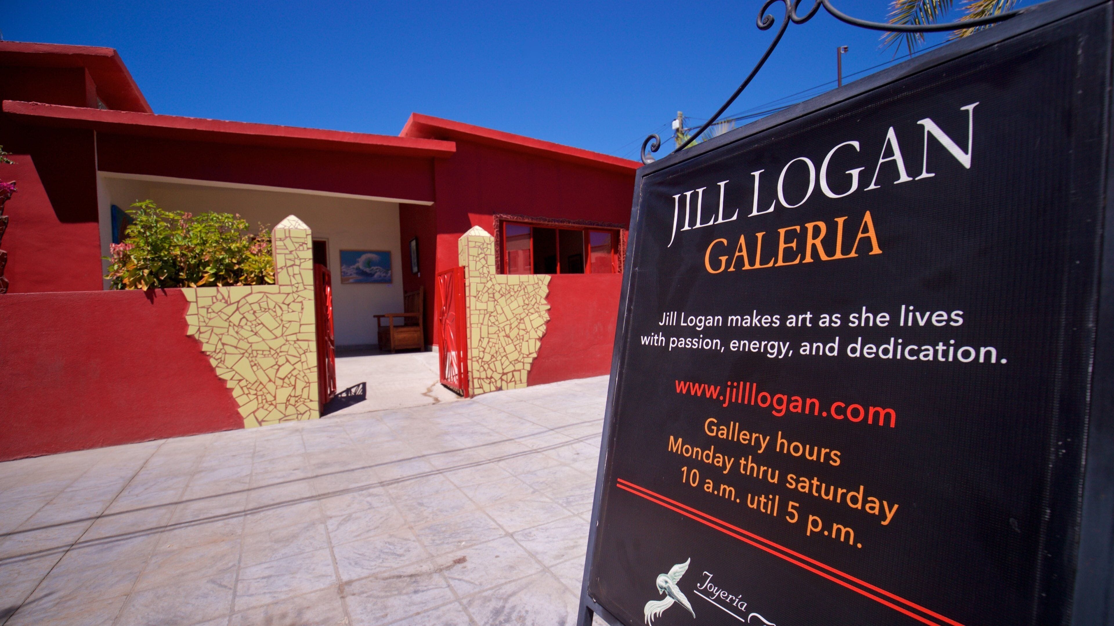 A sign for Jill Logan Gallery with a red building in the background.
