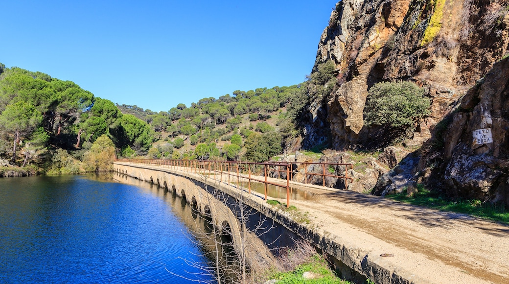 A river with a bridge, a rocky cliff, and a forested hillside.