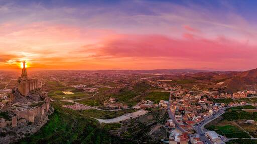 Een panoramisch uitzicht op een stad met een opvallende kathedraal en het omliggende stedelijk landschap tijdens de zonsondergang.