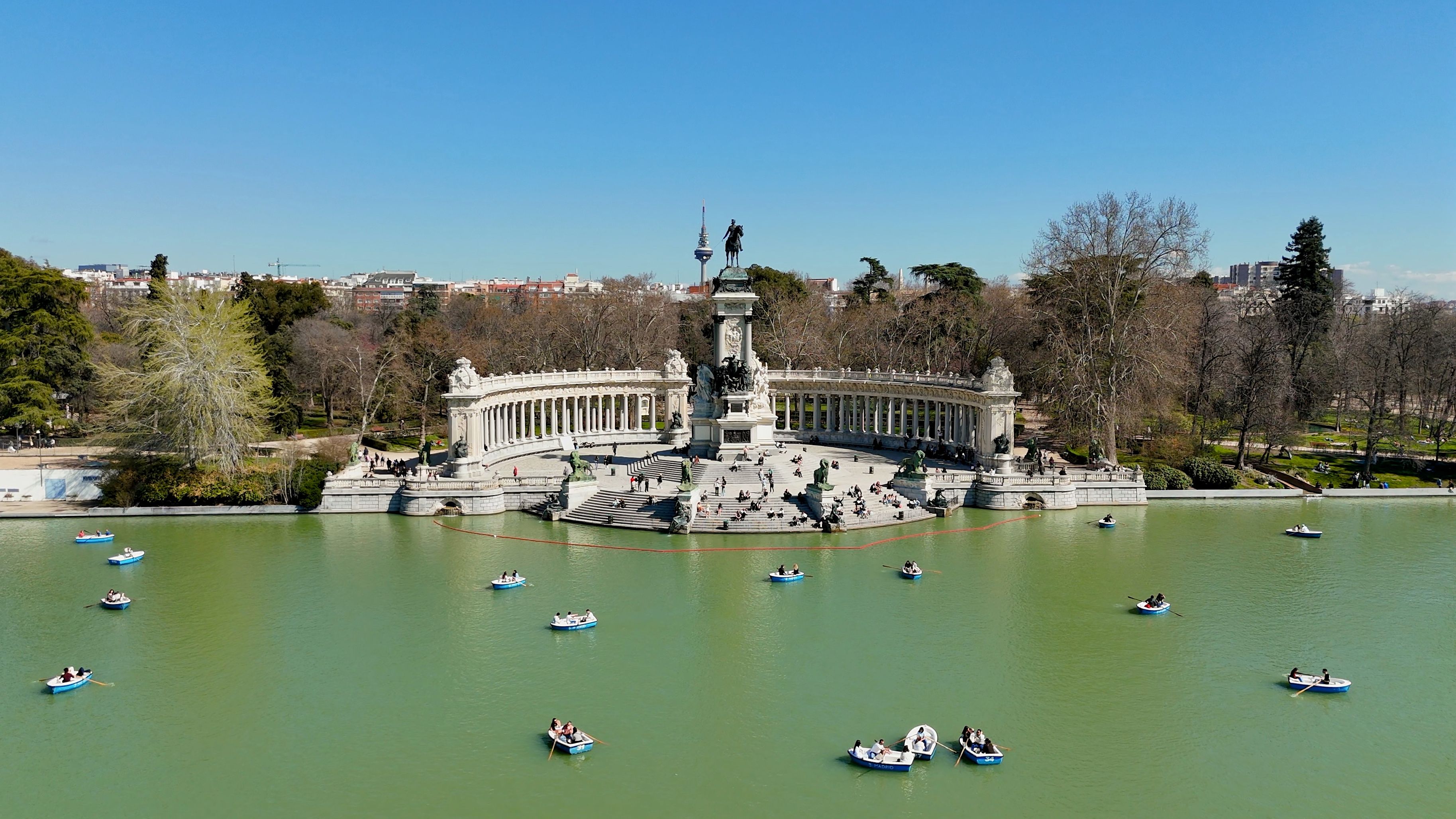 A large fountain with statues and a tower in the center, surrounded by a body of water with several boats.