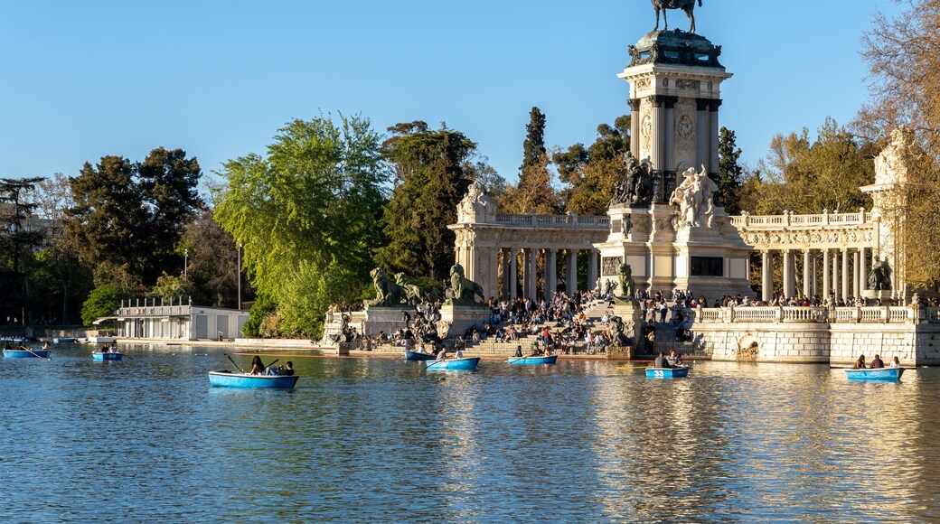 A historic fountain with statues, surrounded by trees and boats on the water.