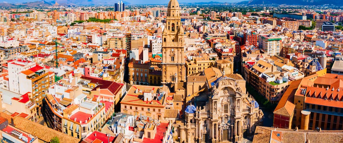 Vista panorâmica de uma cidade com uma catedral imponente, edifícios urbanos densos e um céu azul límpido.