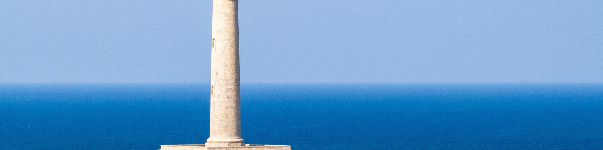 Um farol alto numa falésia rochosa, com o oceano ao fundo.
