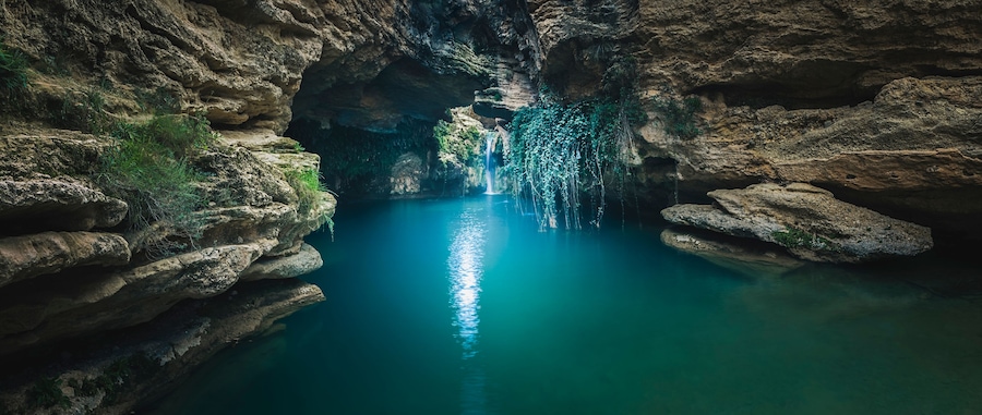Un canyon étroit avec une cascade et une eau d’un bleu cristallin.