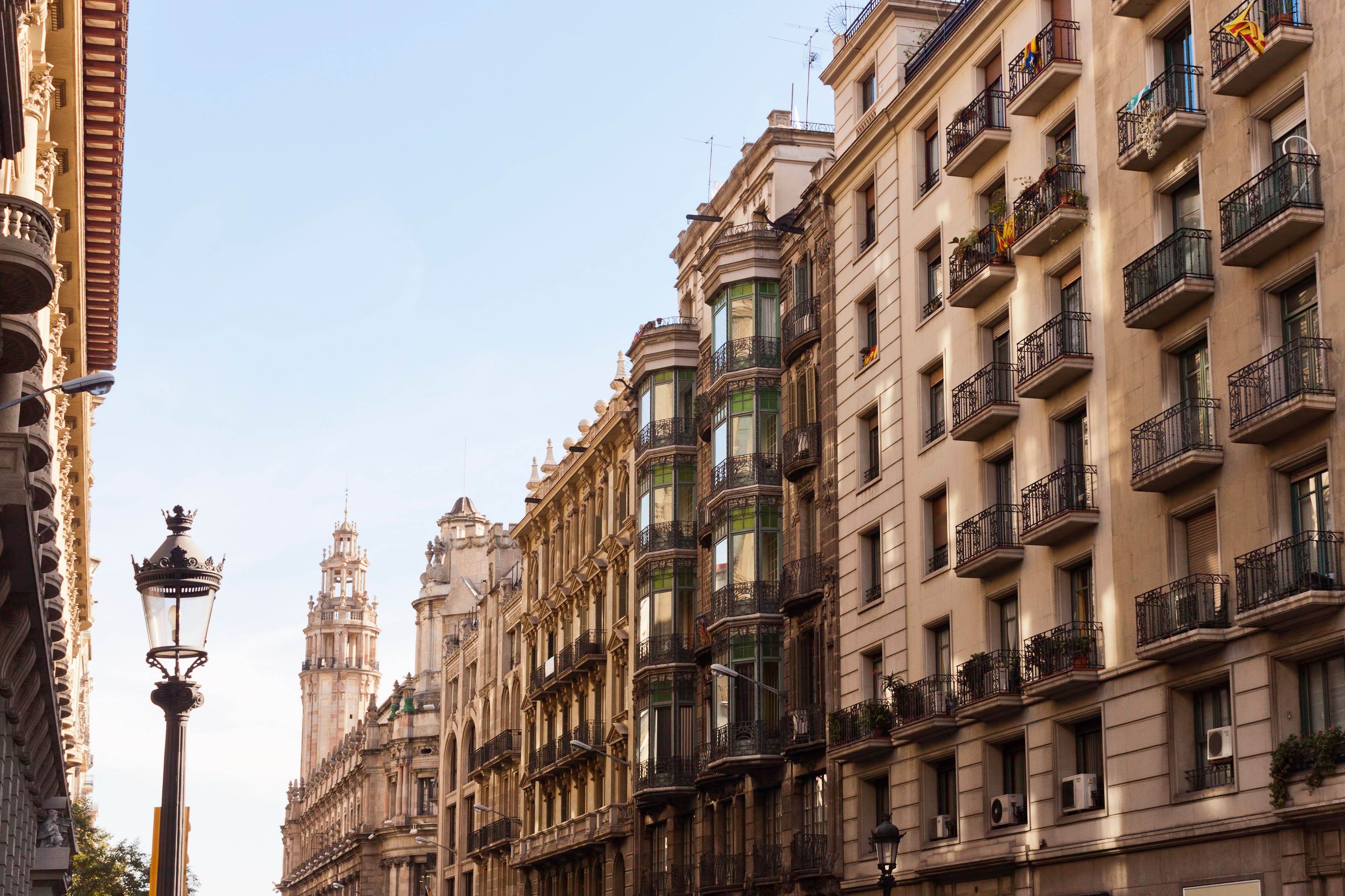 Carrer amb edificis ornamentals, amb balcons amb plantes i baranes decoratives.