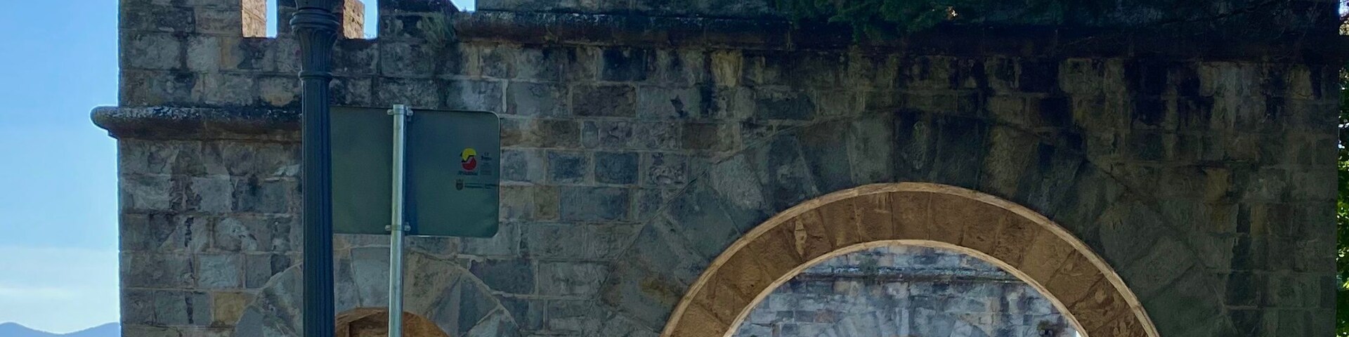 Arcada de pedra com um lampião e uma lixeira em primeiro plano.