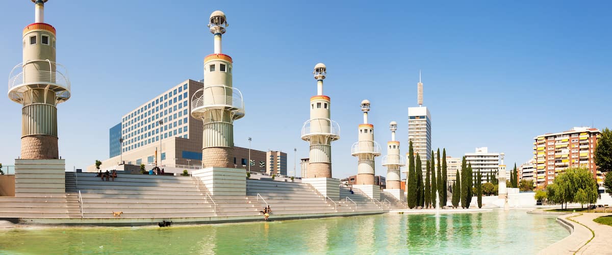 A waterfront promenade with multiple tall towers, a modern building, and a clear blue sky.