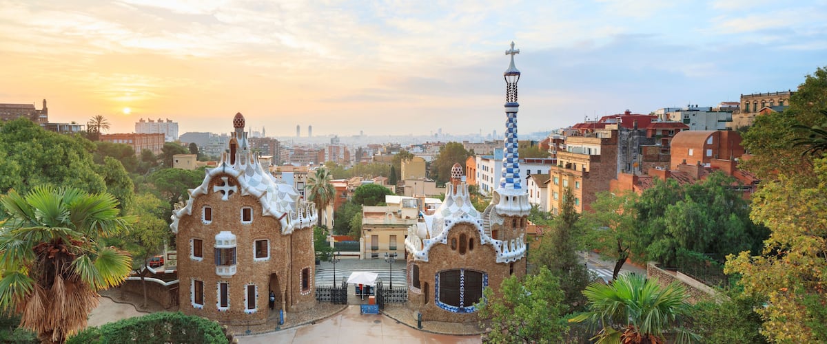 Una veduta di un paesaggio urbano con un edificio caratteristico dotato di una torre con una croce in cima, circondato da vegetazione rigogliosa e altri edifici.