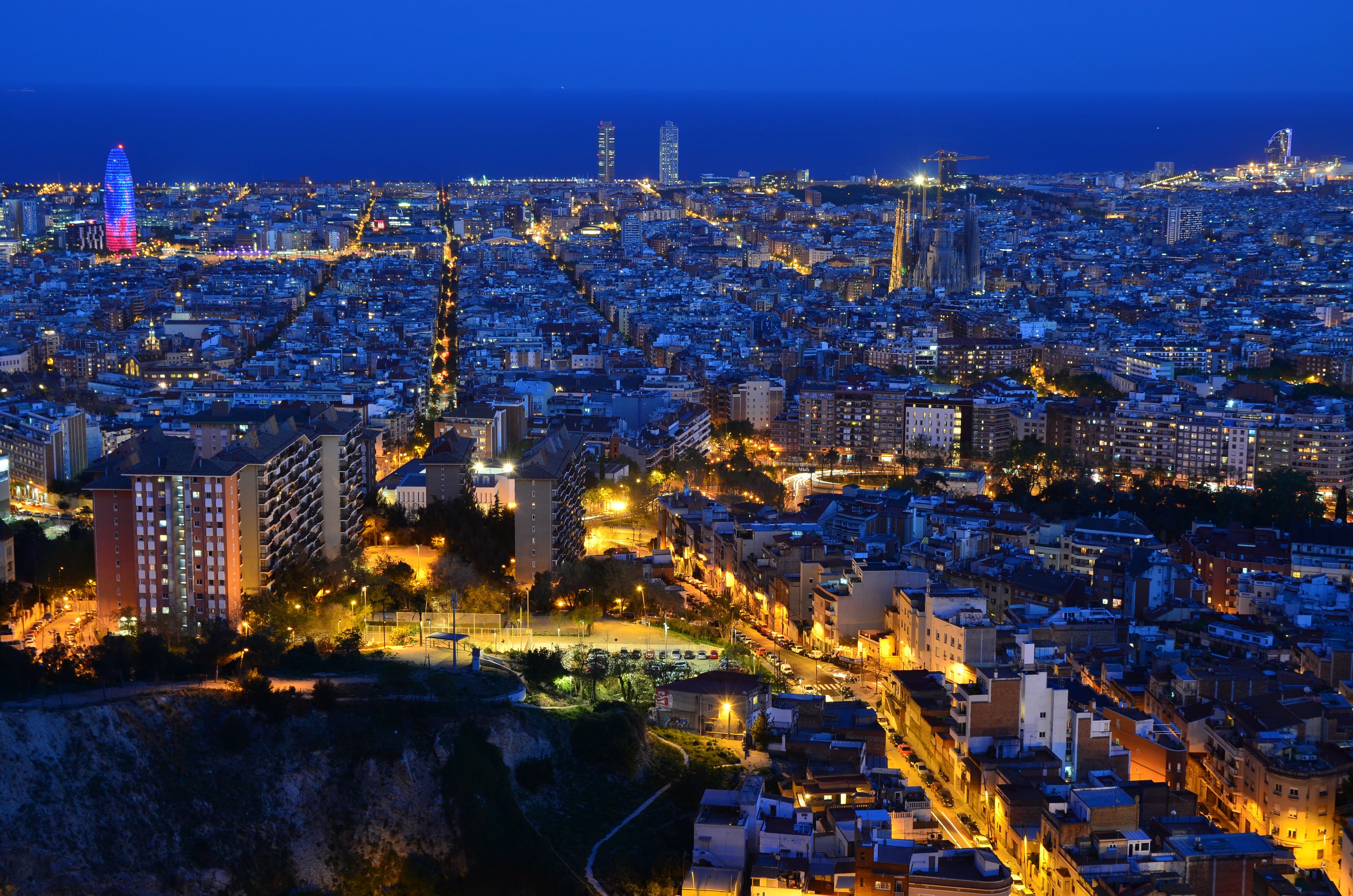 Vista urbana ao entardecer com edifícios iluminados e uma torre imponente.
