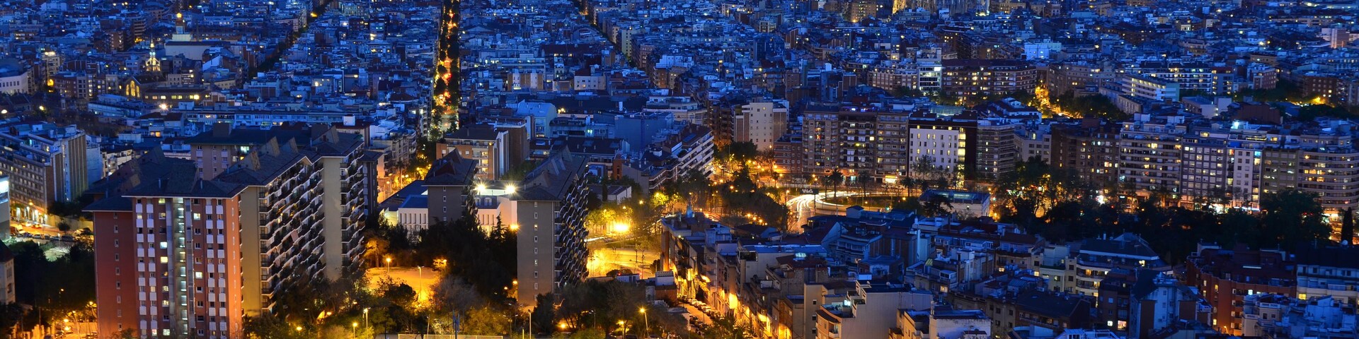 Vista urbana ao entardecer com edifícios iluminados e uma torre imponente.