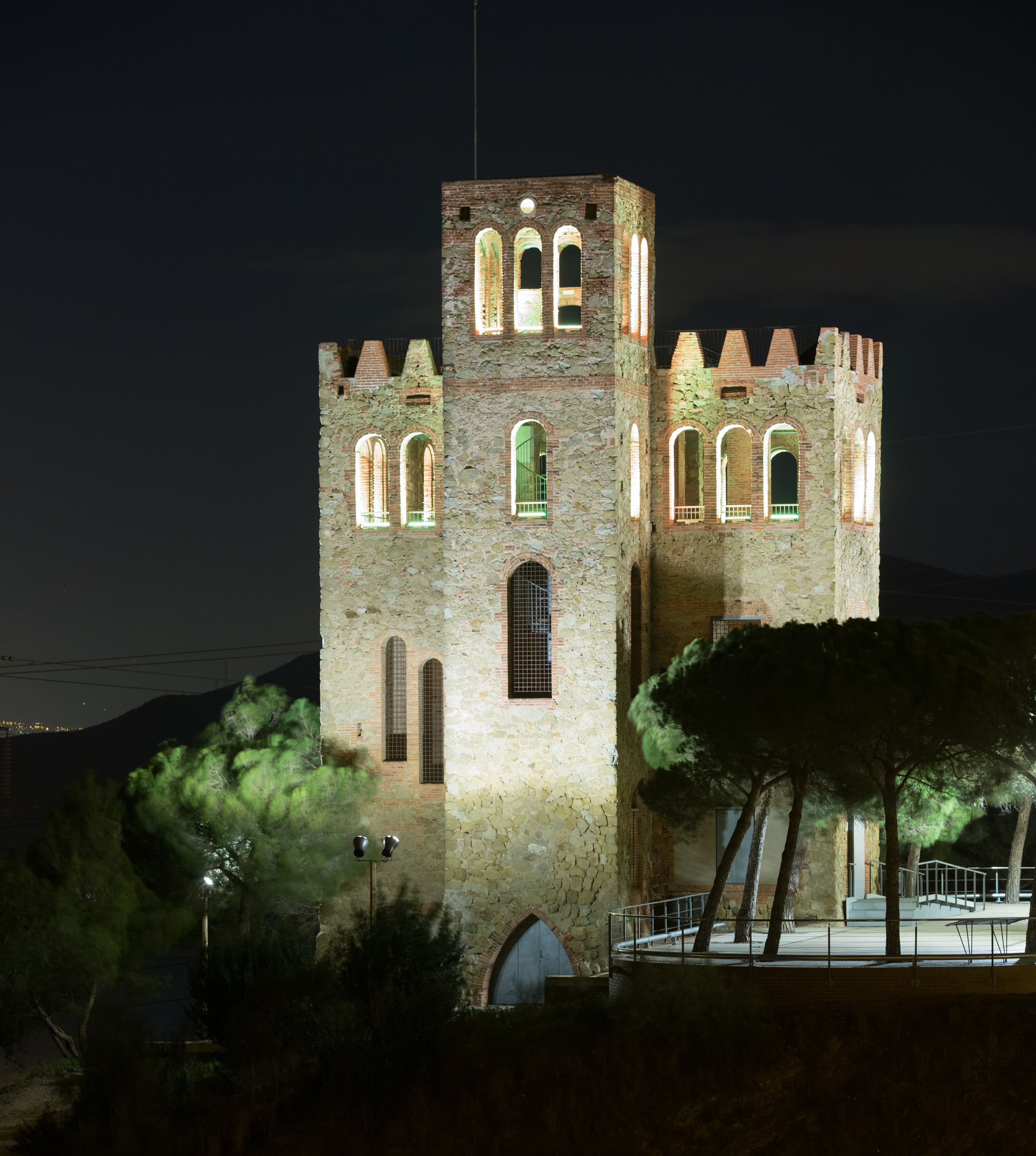 Uma torre de pedra histórica com janelas em arco e varanda, iluminada à noite.