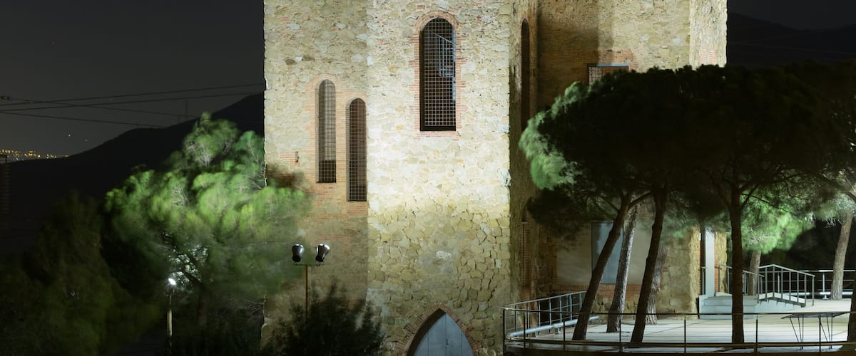 Una torre de piedra histórica con ventanas de arco y un balcón, iluminada por la noche.