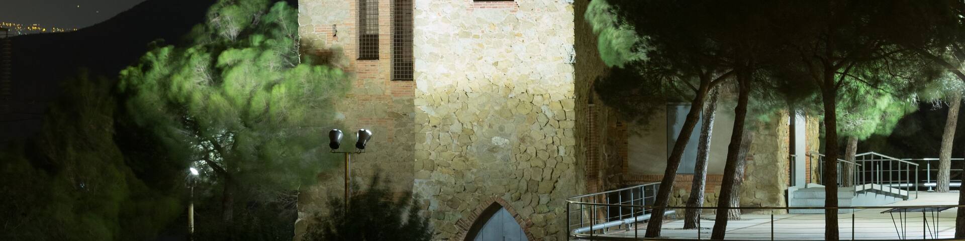 A historic stone tower with arched windows and a balcony, illuminated at night.