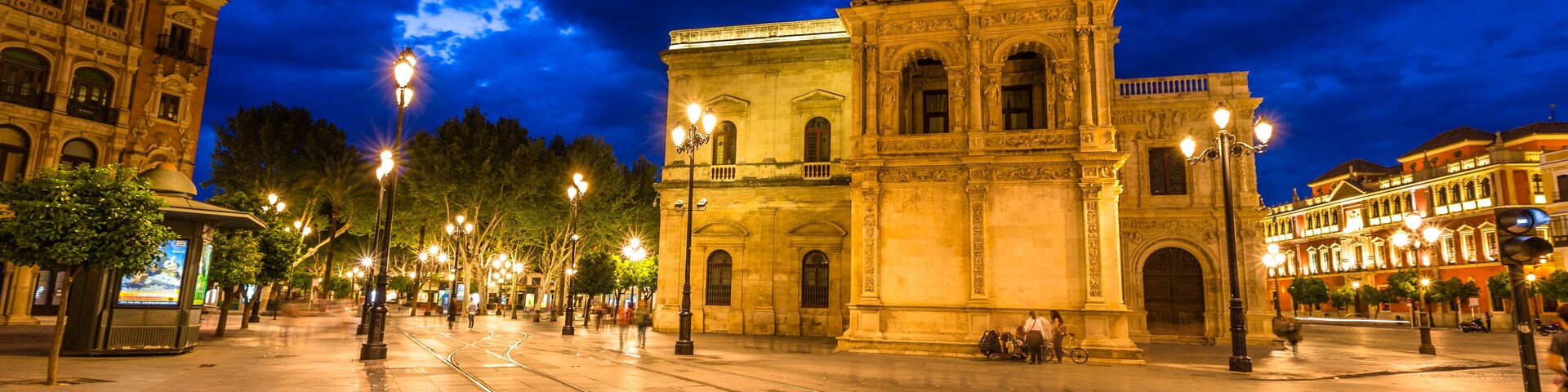 Tram tracks, historic buildings and the streets of the center of Seville illuminated by night. Seville town, Andalusia, Spain.