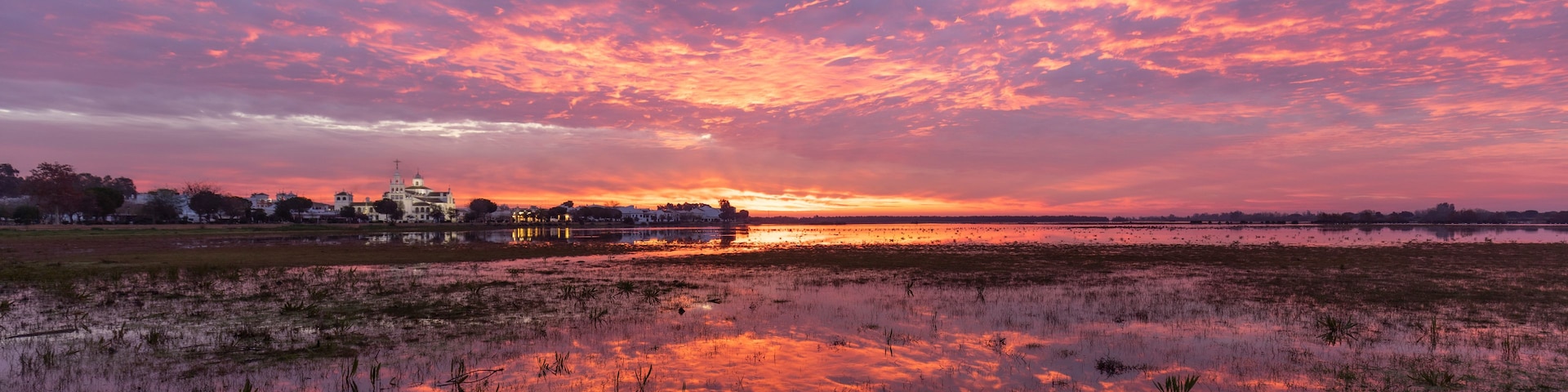 Pôr do sol sobre um campo alagado, com uma igreja ao longe.