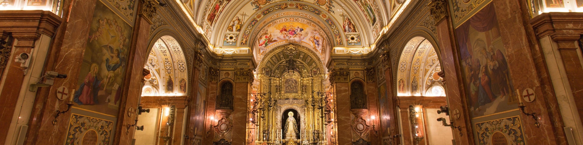 Interior de igreja ornamentado, com um altar central, fileiras de bancos e afrescos detalhados nas paredes e no teto.