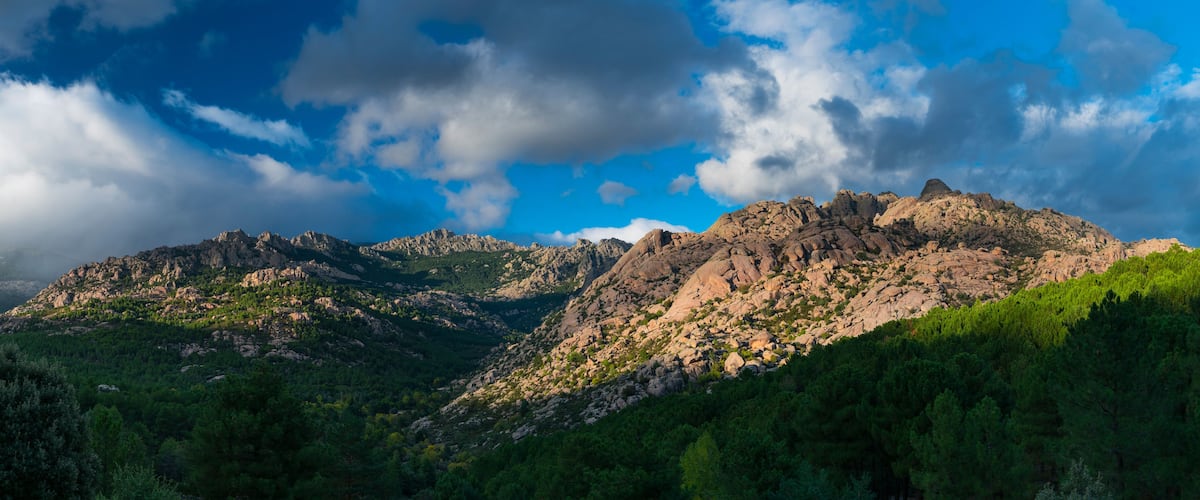 Una cordillera con picos rocosos y densos bosques verdes.