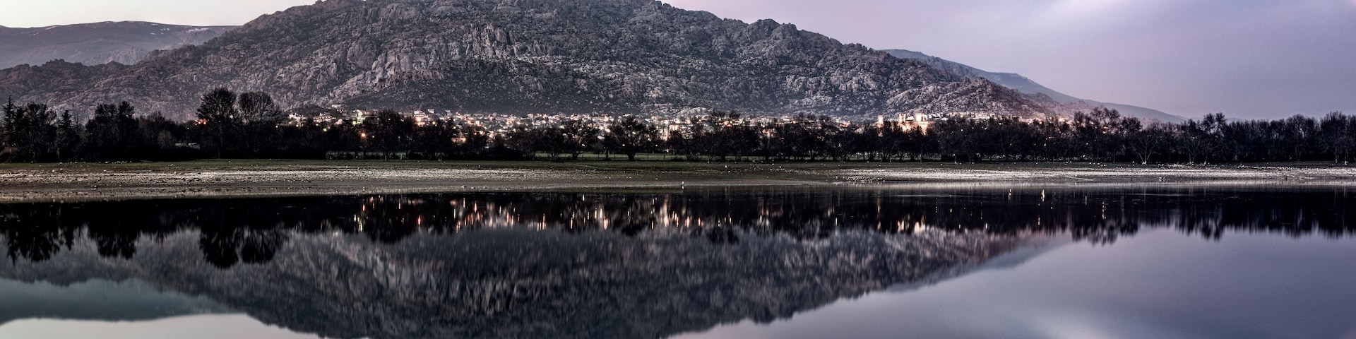 Une chaîne de montagnes se reflétant dans un lac, une ville située dans la vallée en contrebas et un ciel dégagé.