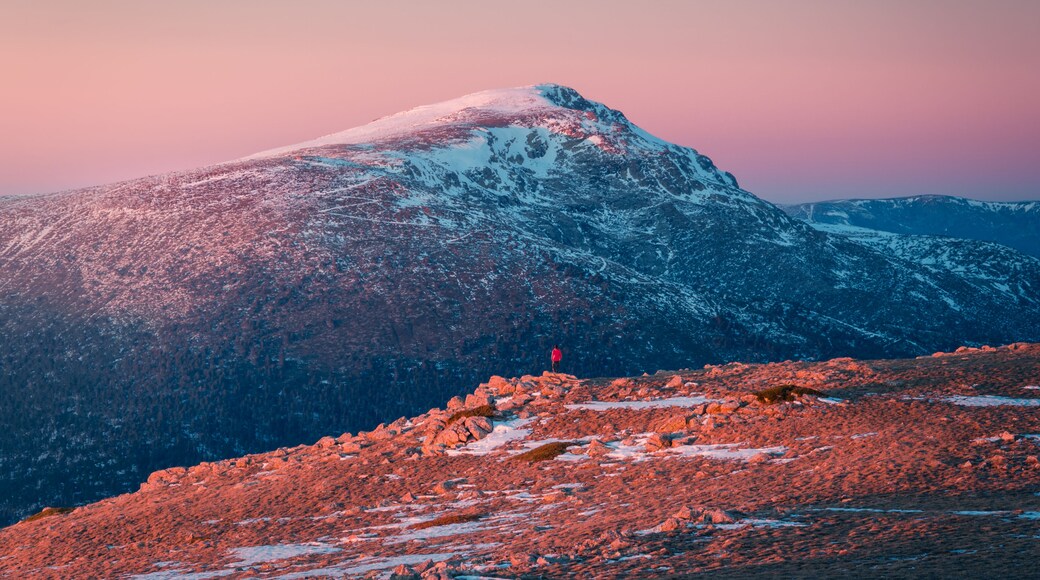 A snow-covered mountain peak with a person standing on a rocky foreground.