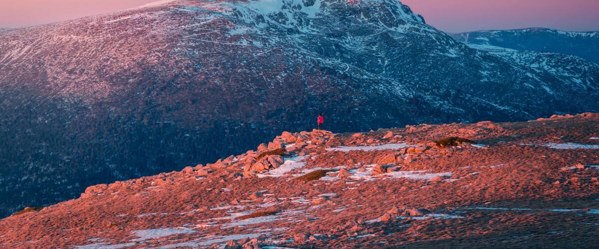 A snow-covered mountain peak with a person standing on a rocky foreground.