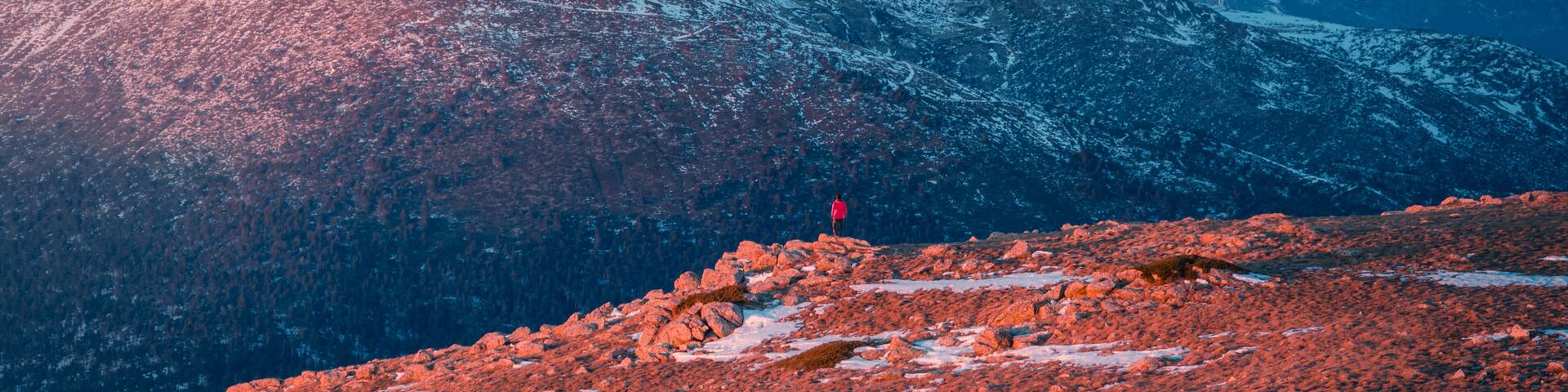 A snow-covered mountain peak with a person standing on a rocky foreground.