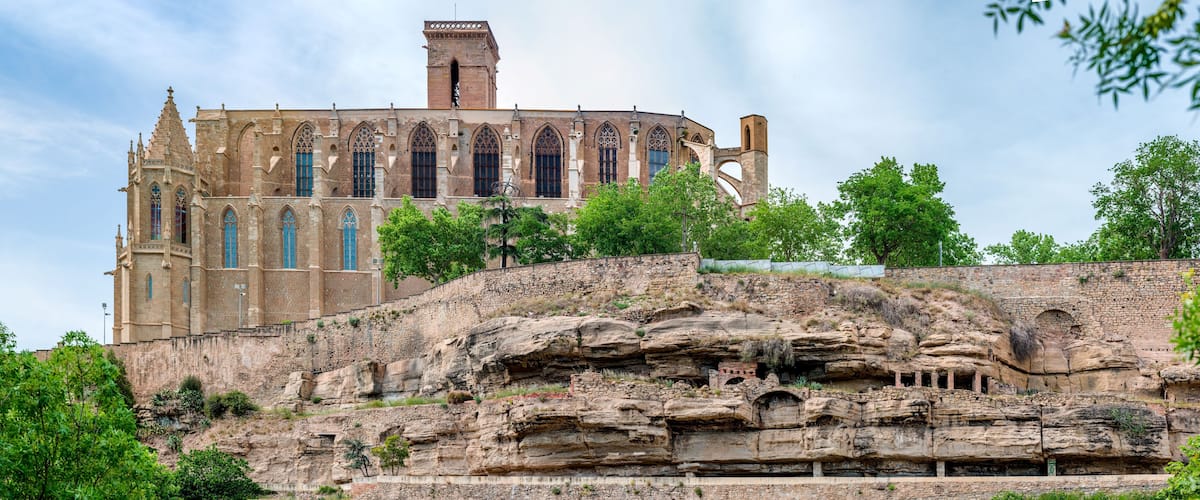 Un bâtiment historique à l’architecture gothique, perché au sommet d’une falaise rocheuse et entouré d’une végétation luxuriante.